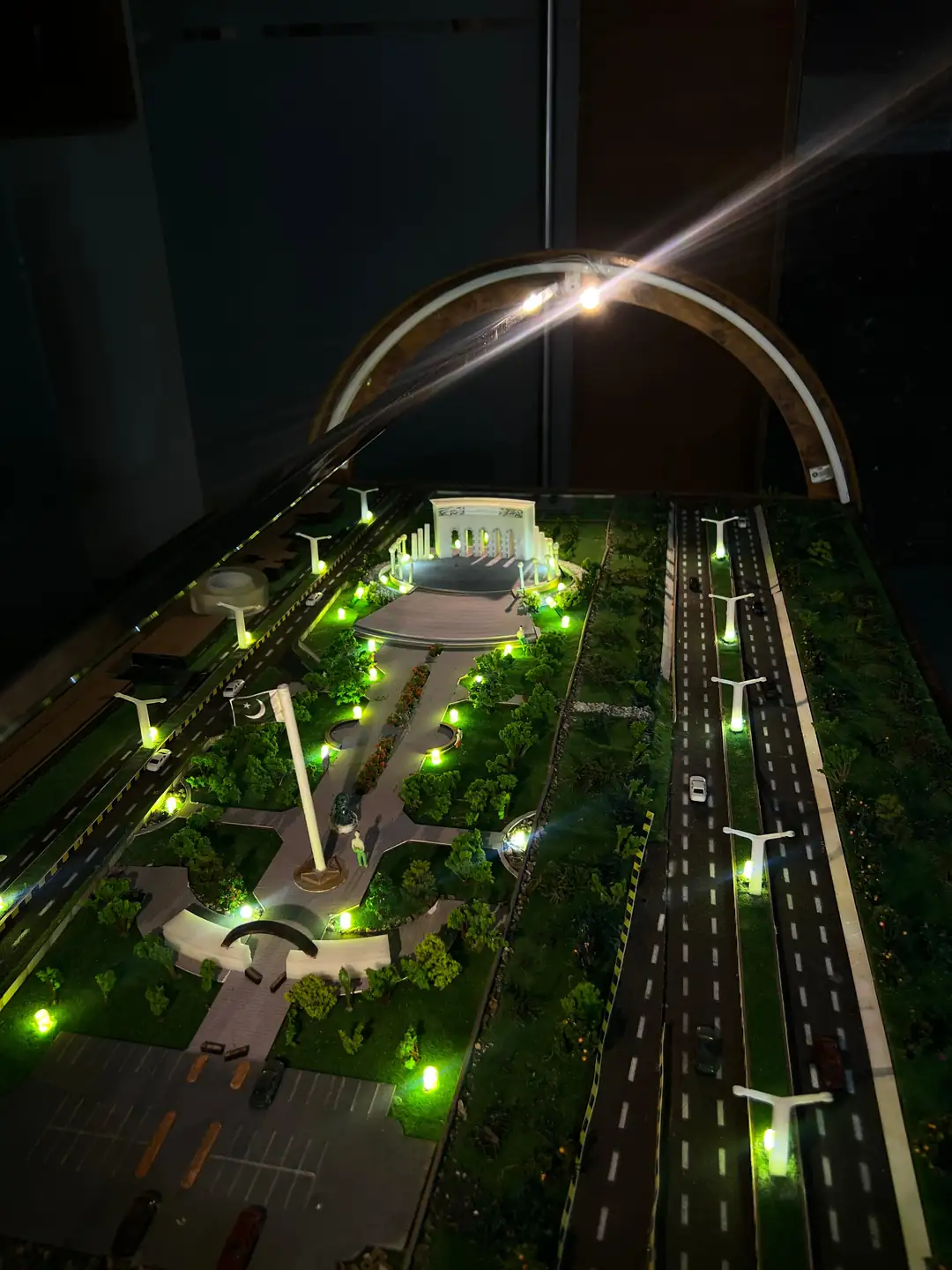 Top view of the illuminated Marka-e-Haq Pakistan monument model showing the arched monument, flag plaza, landscaped walkway, parking and dual carriageway with street lights