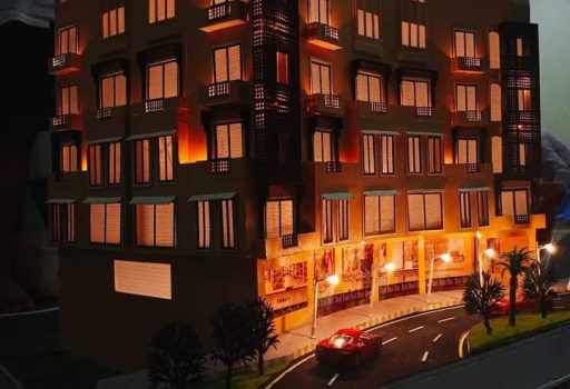 Physical scale model of the Business Center at Riveria, Bahria Phase 7, lit at night with shops at ground level and a road in front